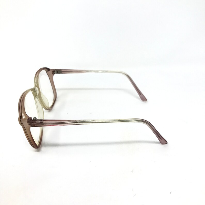 May include: A pair of eyeglasses with a light brown frame and clear lenses. The temples are a gradient, transitioning from light brown to clear. The glasses are set against a white background.