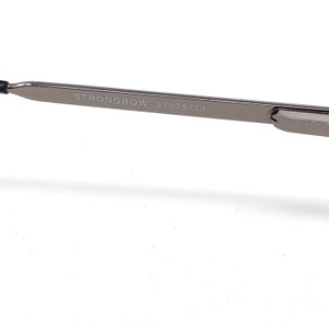 Peut inclure: Gros plan sur une branche de monture de lunettes argent&eacute;e. Le texte "STRONGBOW 21039713" est imprim&eacute; sur la branche. La monture est de conception &eacute;l&eacute;gante et moderne, avec une esth&eacute;tique minimaliste.