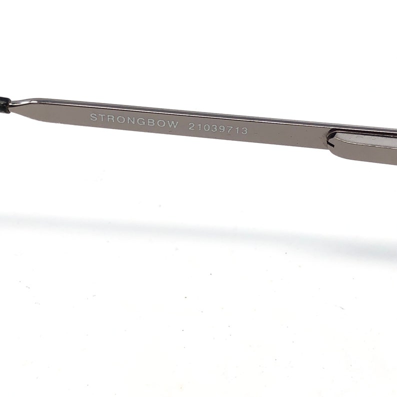 Peut inclure: Gros plan sur une branche de monture de lunettes argent&eacute;e. Le texte "STRONGBOW 21039713" est imprim&eacute; sur la branche. La monture est de conception &eacute;l&eacute;gante et moderne, avec une esth&eacute;tique minimaliste.