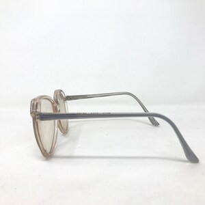 May include: A pair of vintage eyeglasses with a light brown frame and gray temples. The lenses are clear, and the frame has a rectangular shape. The text "RALPH AARON ZINN" is printed on the frame.