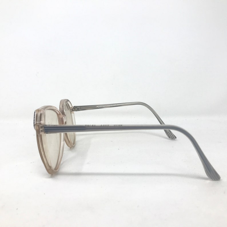 May include: A pair of vintage eyeglasses with a light brown frame and gray temples. The lenses are clear, and the frame has a rectangular shape. The text "RALPH AARON ZINN" is printed on the frame.