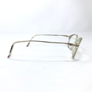 May include: A pair of clear, oval-shaped eyeglasses with a gold metal frame. The frame has a twisted design on the temples.