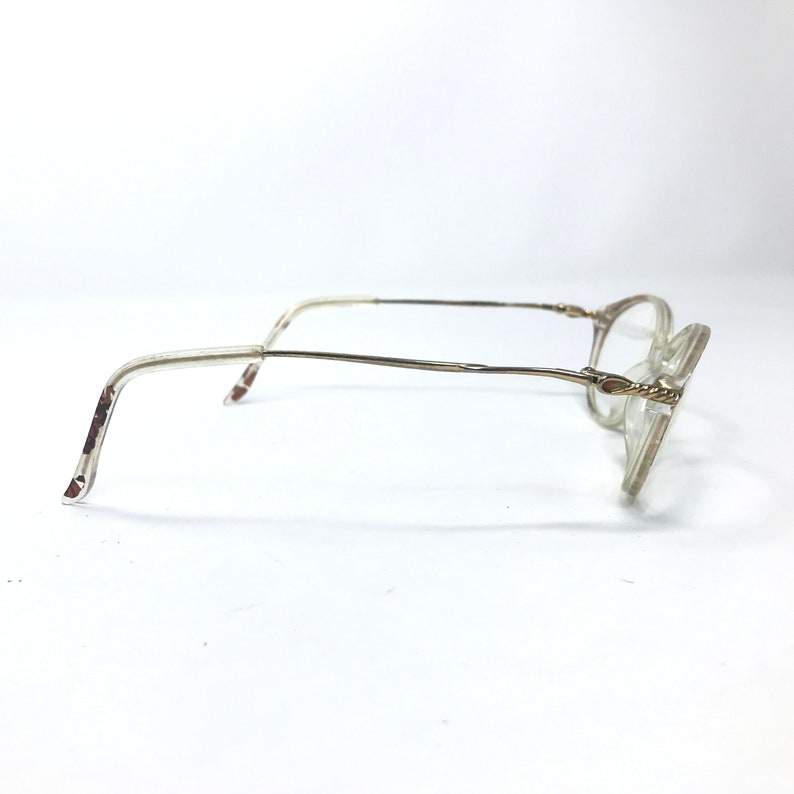 May include: A pair of clear, oval-shaped eyeglasses with a gold metal frame. The frame has a twisted design on the temples.