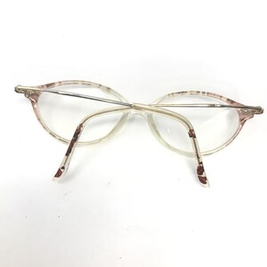 May include: A pair of clear, oval-shaped eyeglasses with a brown and white patterned frame. The glasses have a thin metal bridge and arms.