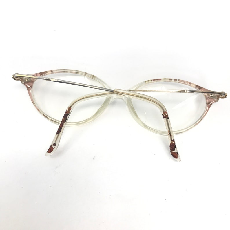 May include: A pair of clear, oval-shaped eyeglasses with a brown and white patterned frame. The glasses have a thin metal bridge and arms.