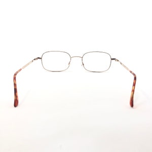 May include: Rectangular spectacles with a thin, silver-coloured metal frame. The arms feature a tortoiseshell pattern. The glasses are set against a white background.