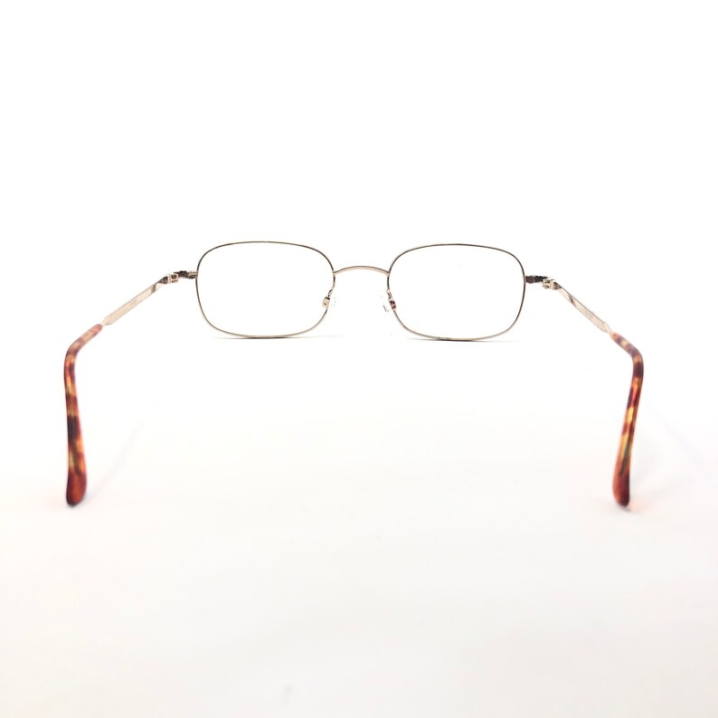 May include: Rectangular spectacles with a thin, silver-coloured metal frame. The arms feature a tortoiseshell pattern. The glasses are set against a white background.