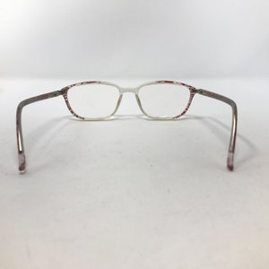 May include: Clear eyeglasses with a rectangular frame and thin, silver-colored arms. The frame has a white base with a red and white striped pattern on the top and sides. The glasses are designed for vision correction.