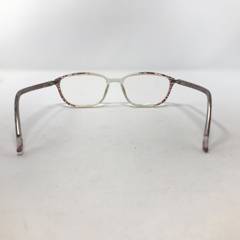 May include: Clear eyeglasses with a rectangular frame and thin, silver-colored arms. The frame has a white base with a red and white striped pattern on the top and sides. The glasses are designed for vision correction.