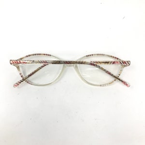 May include: Clear eyeglasses with a patterned design on the frames. The frames have a clear base with a pattern of red, pink, and yellow lines. The lenses are clear and round.