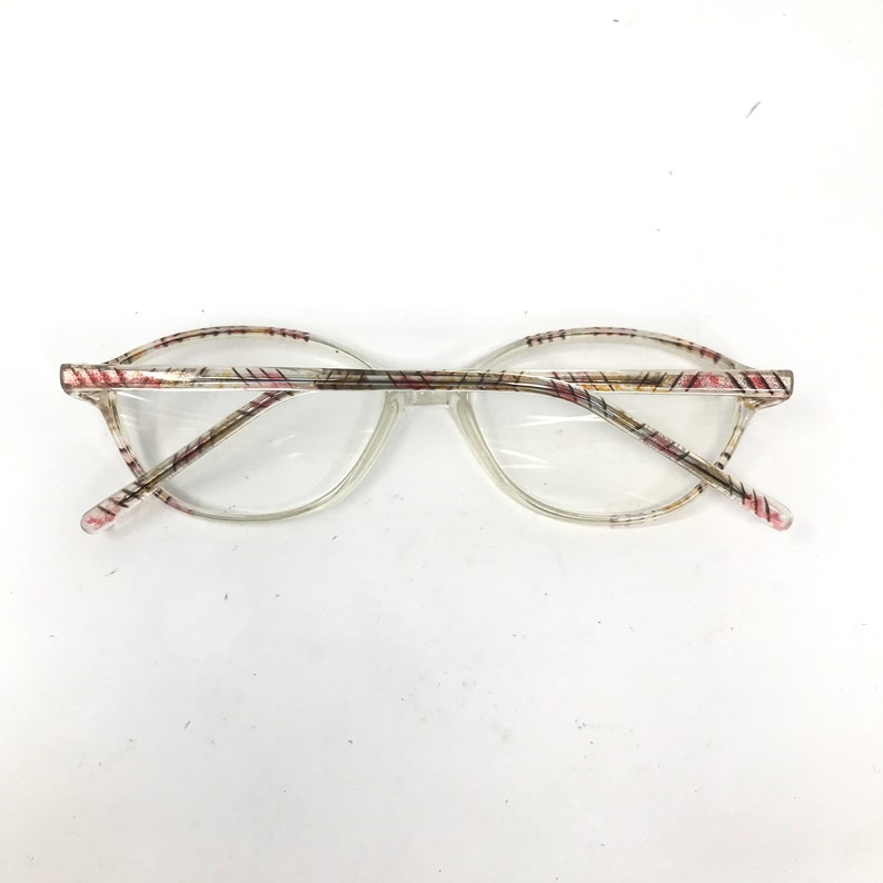 May include: Clear eyeglasses with a patterned design on the frames. The frames have a clear base with a pattern of red, pink, and yellow lines. The lenses are clear and round.