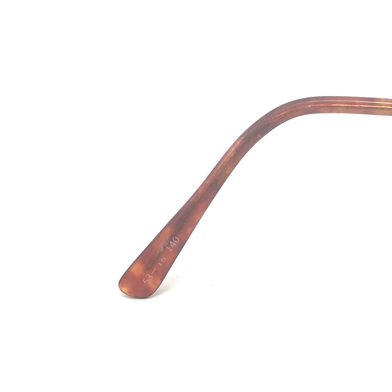 K&ouml;nnte beinhalten: Nahaufnahme eines braunen Brillenb&uuml;gels in Schildpatt-Optik. Der B&uuml;gel ist leicht gebogen und tr&auml;gt die Ma&szlig;e 53-18 140 auf der Innenseite. Der Rahmen hat eine warme braune Farbe mit dunkleren braunen Marmorierungen.