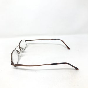 May include: A pair of eyeglasses with a brown metal frame and clear lenses. The glasses have a classic, minimalist design with a rectangular shape. The temples have a tortoiseshell pattern at the ends.