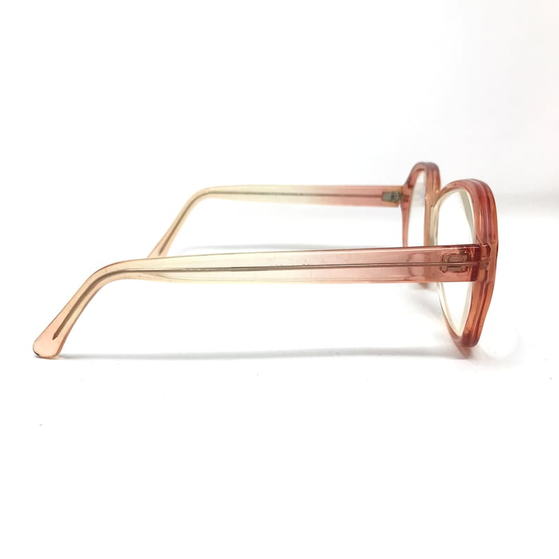 May include: A pair of pink plastic eyeglasses with a gradient fade from light pink to a darker pink. The glasses have a rounded rectangular shape.