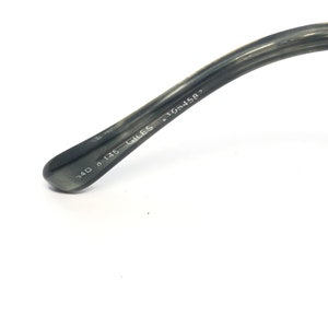 May include: Close-up of the arm of a pair of eyeglasses. The arm is a dark gray color with the text "540 8 145 GILES 41054587" printed in white. The glasses arm is angled towards the top right.