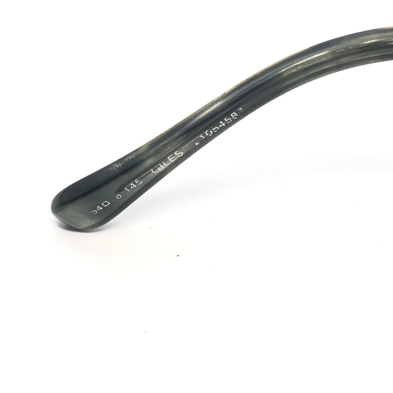 May include: Close-up of the arm of a pair of eyeglasses. The arm is a dark gray color with the text "540 8 145 GILES 41054587" printed in white. The glasses arm is angled towards the top right.