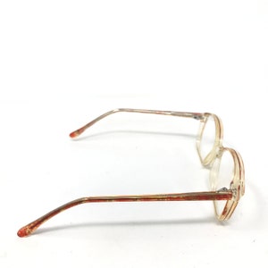 May include: A pair of vintage eyeglasses with a clear, rectangular frame and thin, gold-colored metal arms. The arms have a reddish-brown pattern. The glasses are set against a white background.