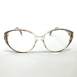 May include: Clear plastic eyeglasses with a brown and gold patterned frame.