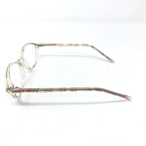 May include: Clear eyeglasses with round lenses and patterned temples. The temples feature a repeating pattern of red, yellow, and brown lines. The glasses are set against a white background.