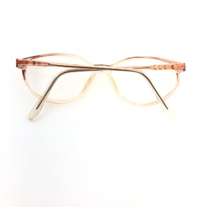 May include: Vintage eyeglasses with a light brown frame and clear lenses. The glasses have an oval shape and a thin metal bridge. The temples are a lighter shade of brown and extend to the ear pieces.