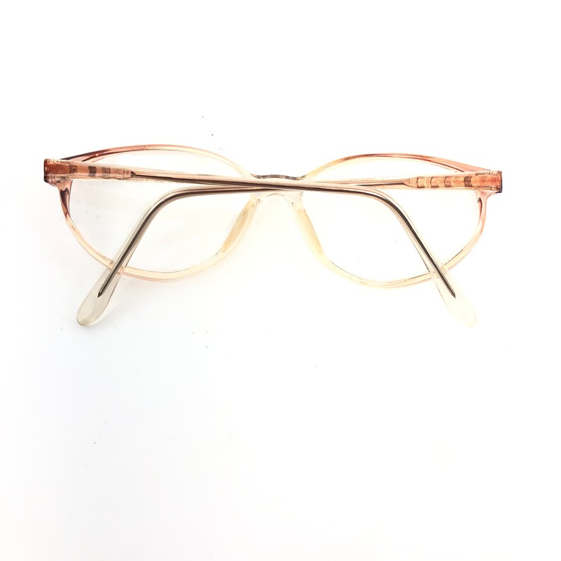 May include: Vintage eyeglasses with a light brown frame and clear lenses. The glasses have an oval shape and a thin metal bridge. The temples are a lighter shade of brown and extend to the ear pieces.