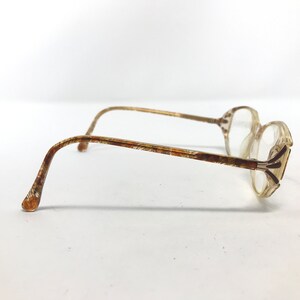 May include: A pair of vintage eyeglasses with a clear, rectangular frame and patterned temples. The temples and frame accents have a brown and gold pattern. The lenses are clear, and the overall style is retro.