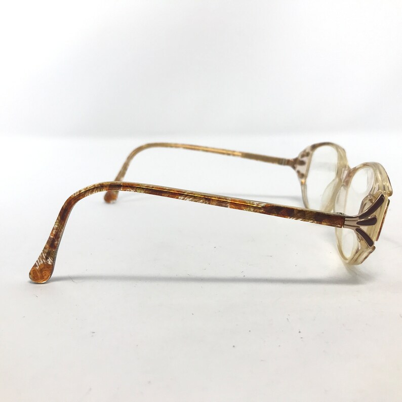 May include: A pair of vintage eyeglasses with a clear, rectangular frame and patterned temples. The temples and frame accents have a brown and gold pattern. The lenses are clear, and the overall style is retro.