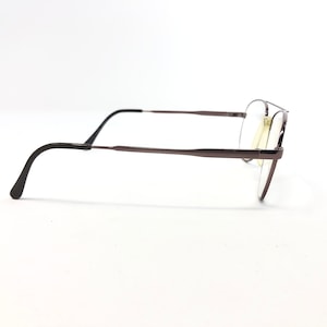 May include: A pair of eyeglasses with a dark brown metal frame. The glasses have a classic aviator style with a double bridge and clear lenses. The earpieces are black and curve down to fit behind the ears.