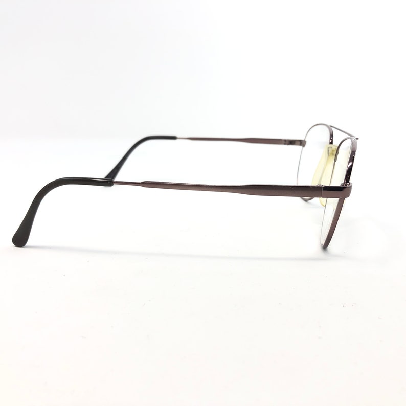May include: A pair of eyeglasses with a dark brown metal frame. The glasses have a classic aviator style with a double bridge and clear lenses. The earpieces are black and curve down to fit behind the ears.