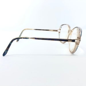 May include: Vintage eyeglasses with a gold-tone frame and clear lenses. The temples feature a blue and green marbled pattern. The frames have a geometric design at the bridge and the lenses are round.