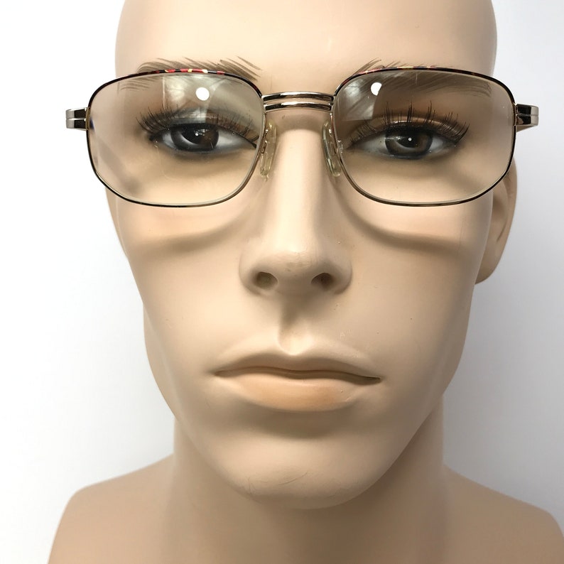 May include: Gold-rimmed eyeglasses with clear lenses and a red and black patterned frame.