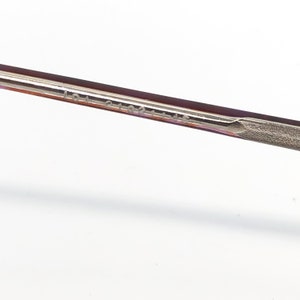 K&ouml;nnte beinhalten: Nahaufnahme eines Teils des Brillenrahmens. Der Rahmen hat eine dunkelburgunder Farbe mit einem silberfarbenen Metallb&uuml;gel. Der Text "LDJ 2102 145" ist auf dem B&uuml;gel aufgedruckt.
