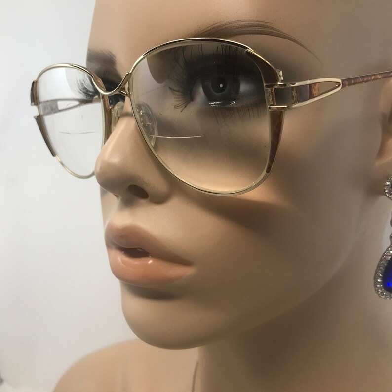 K&ouml;nnte beinhalten: Goldrandbrille mit Farbverlauf. Die Brille hat ein klassisches, &uuml;bergro&szlig;es Design mit rechteckiger Form. Die Fassungen weisen ein Schildpattmuster an den B&uuml;geln auf. Die Gl&auml;ser sind klar mit einem leichten Farbton.