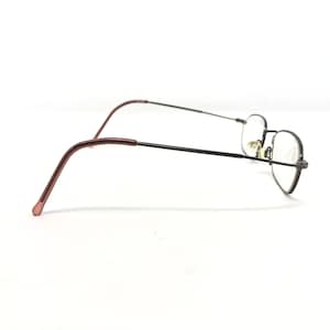 Puede incluir: Un par de gafas con una montura fina de metal negro y lentes transparentes. Las patillas son de color marr&oacute;n rojizo. Las gafas est&aacute;n sobre un fondo blanco.