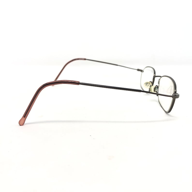 Puede incluir: Un par de gafas con una montura fina de metal negro y lentes transparentes. Las patillas son de color marr&oacute;n rojizo. Las gafas est&aacute;n sobre un fondo blanco.