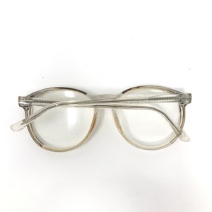Puede incluir: Gafas transparentes con montura redonda y clara. La montura es de color claro. Las gafas tienen un dise&ntilde;o cl&aacute;sico, con puente y patillas. Las lentes son claras y el estilo general es sencillo y funcional. Adecuadas para el uso diario.
