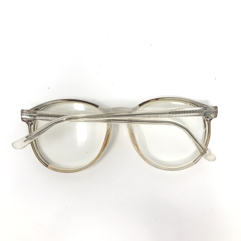 Puede incluir: Gafas transparentes con montura redonda y clara. La montura es de color claro. Las gafas tienen un dise&ntilde;o cl&aacute;sico, con puente y patillas. Las lentes son claras y el estilo general es sencillo y funcional. Adecuadas para el uso diario.