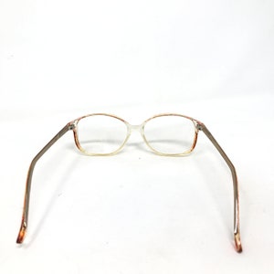 May include: Clear eyeglasses with a rectangular frame and brown accents. The temples are a silver-gray color. The glasses are set against a white background.