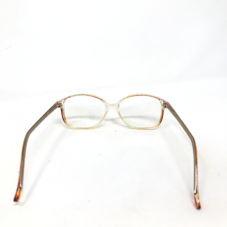 May include: Clear eyeglasses with a rectangular frame and brown accents. The temples are a silver-gray color. The glasses are set against a white background.