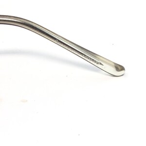 May include: Close-up of a clear eyeglass arm with the text "OceanSaver 1000472 CE" printed on the side. The arm is curved and has a rounded tip. The background is white.