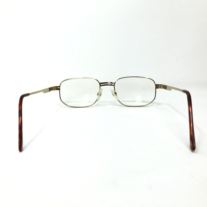 May include: Gold-tone metal rectangular eyeglasses with brown tortoise shell temple arms.