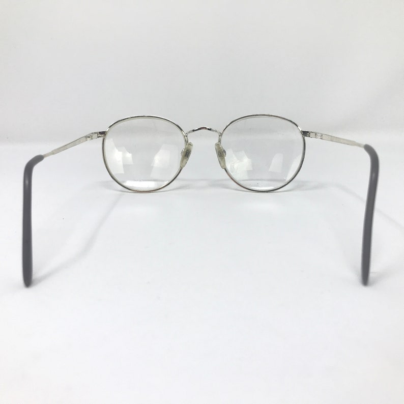 Peut inclure: Lunettes &agrave; monture argent&eacute;e avec verres ronds. Les lunettes ont un design classique avec une monture en m&eacute;tal fin et des branches gris fonc&eacute;. Les verres sont clairs, sur fond blanc.