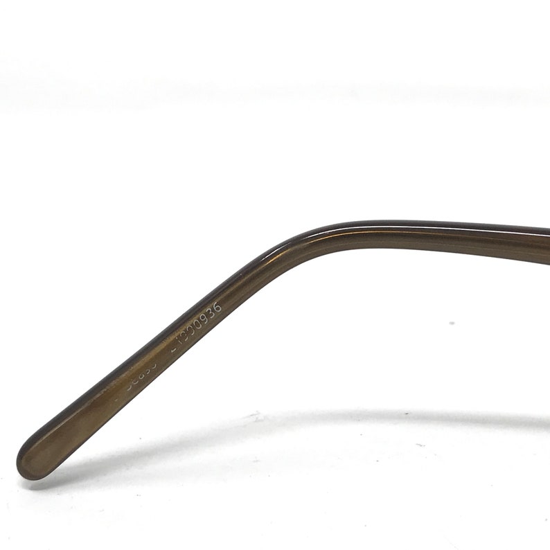 May include: Close-up of the temple arm of eyeglasses. The arm is a translucent brown color with the text "SE035 - 1300936" printed on the side. The arm curves gently and has a rounded tip.
