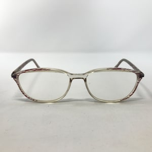 May include: Clear eyeglasses with a thin, oval frame. The rims feature a red and white striped pattern. The temples are a dark brown color. The glasses are set against a white background.