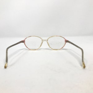 K&ouml;nnte beinhalten: Eine Brille mit ovalen, transparenten Gl&auml;sern, einem rosafarbenen Rahmen und silbernen B&uuml;geln.