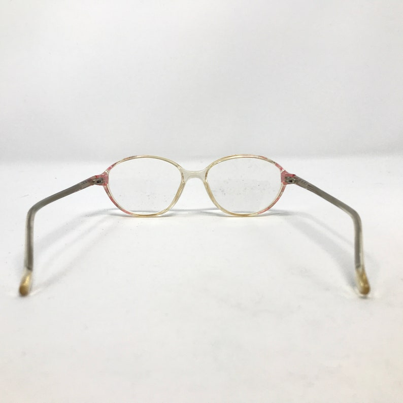 K&ouml;nnte beinhalten: Eine Brille mit ovalen, transparenten Gl&auml;sern, einem rosafarbenen Rahmen und silbernen B&uuml;geln.