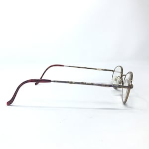 May include: A pair of gold-toned spectacles with a brown tortoiseshell temple. The glasses have a round frame and a thin, twisted metal bridge.