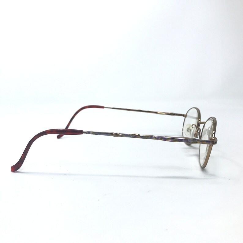 May include: A pair of gold-toned spectacles with a brown tortoiseshell temple. The glasses have a round frame and a thin, twisted metal bridge.