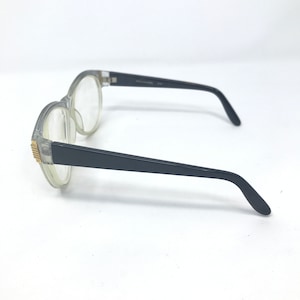 May include: Clear plastic framed glasses with black arms. The glasses have a rounded shape and gold accents on the frame.