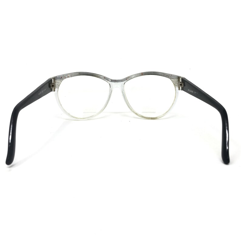 May include: Clear eyeglasses with a rounded frame and black temples. The frame has a speckled design along the top. The lenses are clear, and the glasses are open, displaying the interior of the frame.
